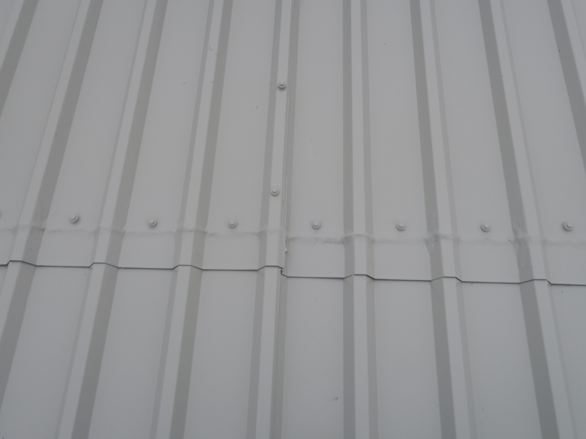 Image showing a steel profiled roof, completed repair detail. The exposed edge of the lap remains open, with the butyl weathering strip positioned beneath the new repair section.